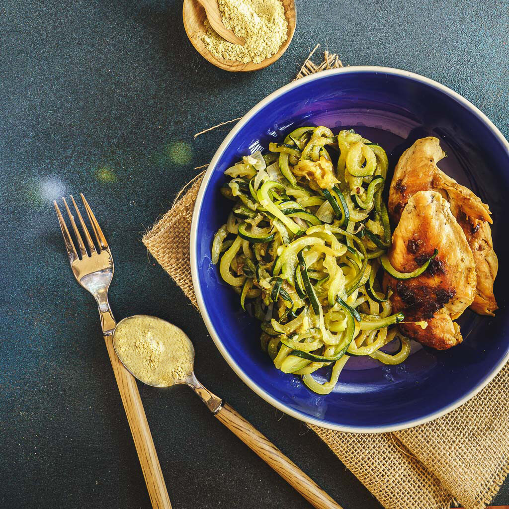 une assiette de spaghetti de courgette présentée avec de le la graine de fenouil en poudre et du blanc de poulet