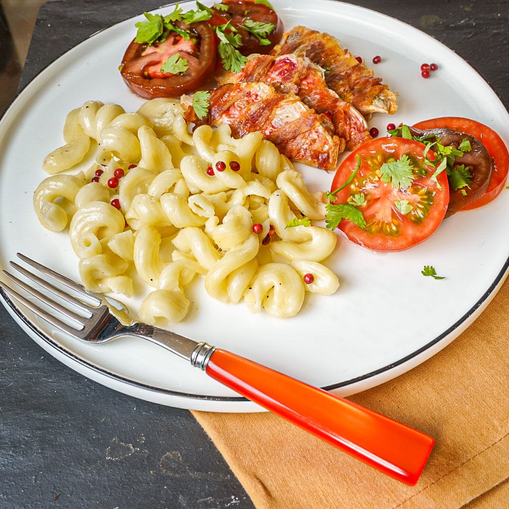 Filets de rouget barbet enroulés de pancetta servis avec des tomates anciennes et des pâtes au beurre et aux baies roses