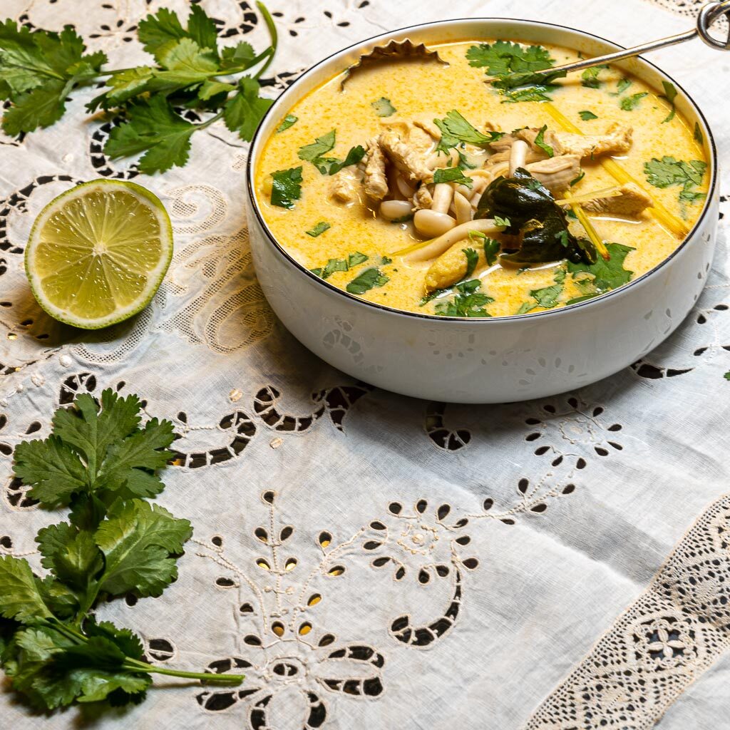 Bol de soupe thaïe au curry , quelques feuilles de coriandre éparpillées et un demi lime