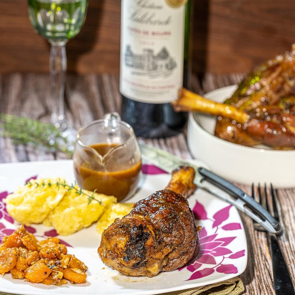 une assiette de souris d'agneau confite au miel de litchi bio présentée avec des pommes de terre et des carottes